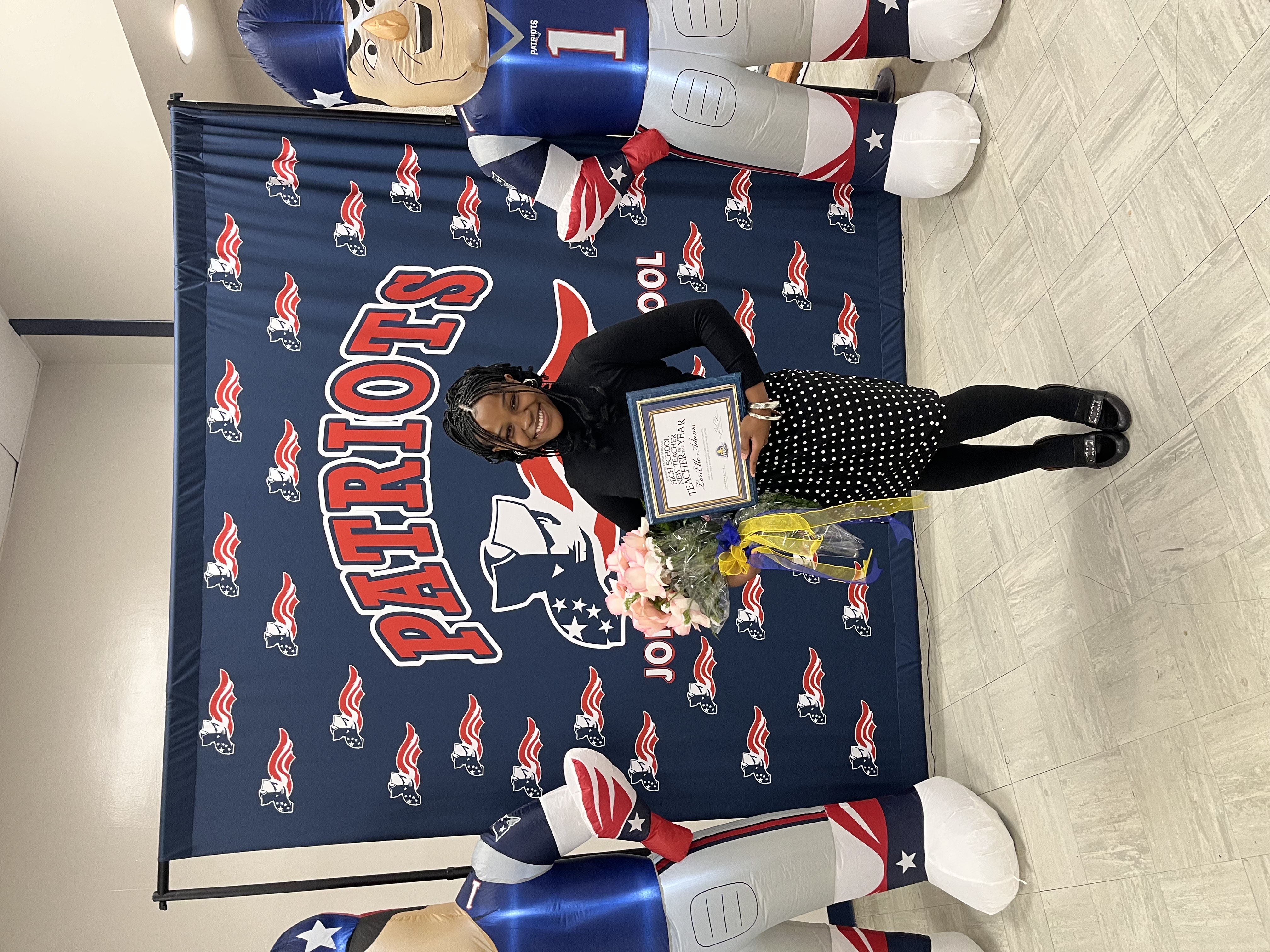 LoriElle holding certificate in front of Patriots back drop.