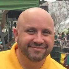 Headshot of Faimon Roberts. He is wearing a yellow shirt and smiling.